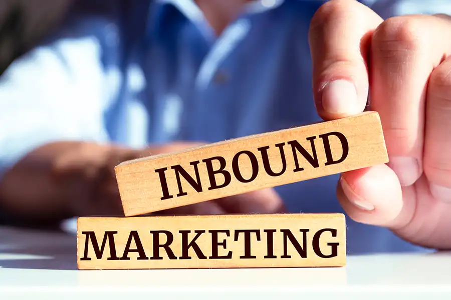 A person’s hand is stacking two wooden blocks labeled “INBOUND” and “MARKETING,” highlighting the concept of inbound marketing against a softly blurred background.