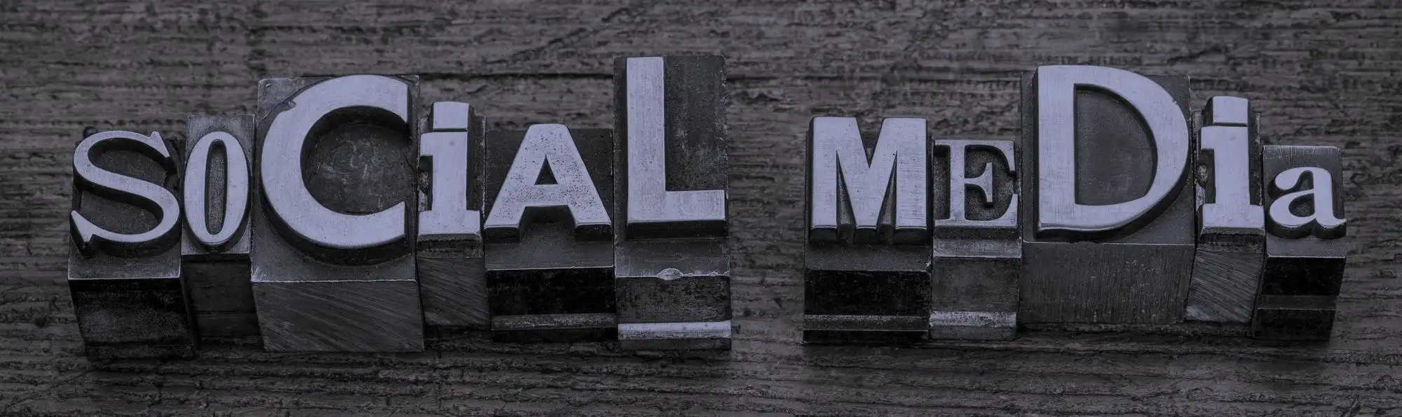 Vintage metal letterpress blocks spell out SOCIAL MEDIA on a textured, dark wooden background. The artistic arrangement highlights the benefits of social media for manufacturers looking to connect and engage in creative ways.